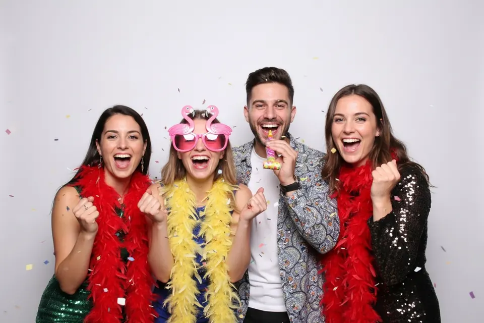 Gruppenfoto aus der Fotobox: vier Personen mit Federboas und Partybrille vor weißem Hintergrund